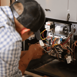 The image shows a close-up of an HVAC experts working on wires of an HVAC unit.